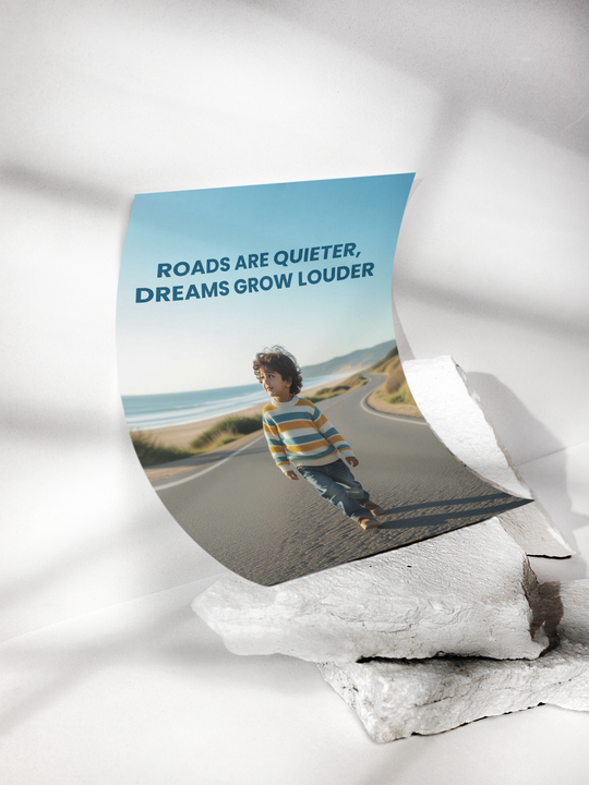 Poster with a child on a road by the sea and text 'Roads are quieter, dreams grow louder' on a white background.