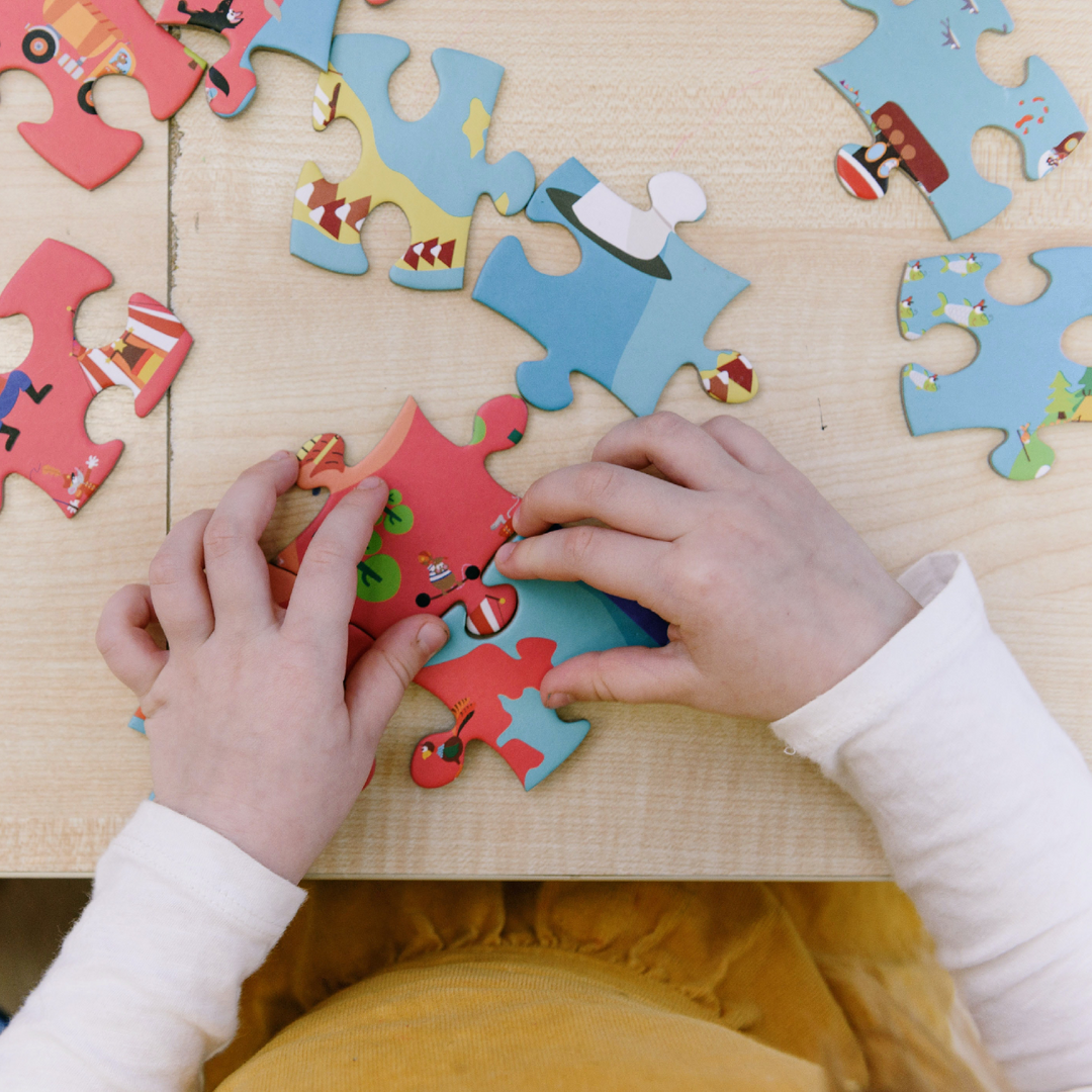 Custom photo jigsaw puzzle gift printed on premium MDF wood, showing hands assembling colorful personalized puzzle pieces on a wooden table. Printed by printlagoon