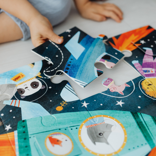 Child assembling colorful space-themed custom photo jigsaw puzzle pieces on a table, featuring cartoon animals and rocket illustrations.